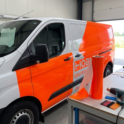 Échenillage d'un lettrage découpé dans du film adhésif fluorescent orange Oracal 6510 sur table d'atelier