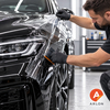 Installateur die transparante Arlon PPF met een zwarte rakel over de voorzijde van een auto spant